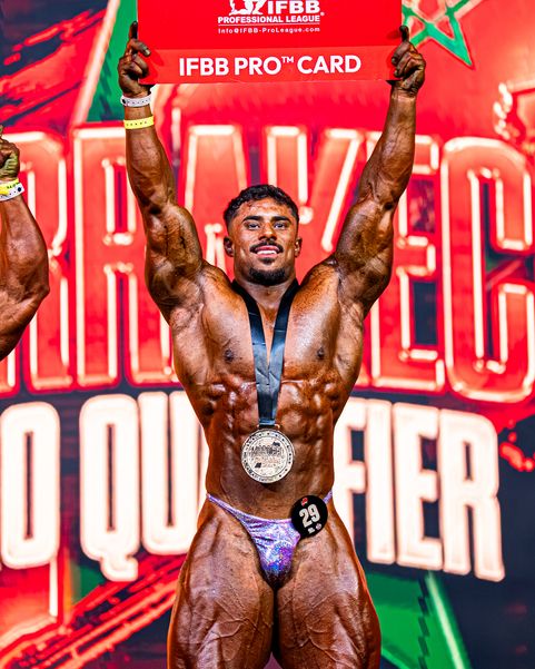 Coachen lyfter sitt IFBB Pro Card över huvudet på tävlingsscenen.